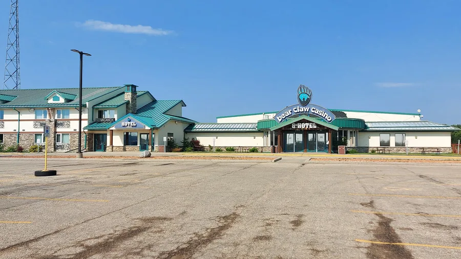 Bear Claw Casino and its hotel wing with green roofs, seen across the parking lot on a summer day